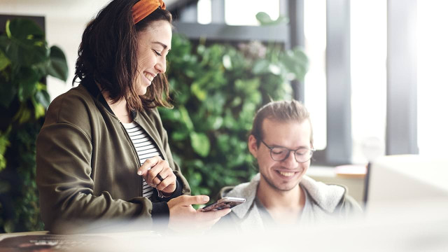 Zwei Teammitglieder bei DOTS – Die Agentur in Freiburg lachen und arbeiten gemeinsam in einer modernen, grünen Arbeitsumgebung. Das Bild vermittelt Teamgeist, Freude an der Zusammenarbeit und eine offene, kreative Unternehmenskultur.